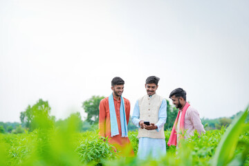 three young indian farmer holding smartphone together at green agricultural field