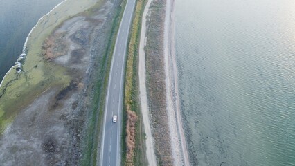 Aerial view of a lone white car driving on a rural highway surrounded by lakes.