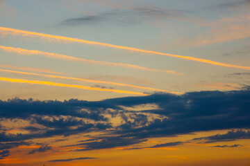 A sunset over Ukraine, where the sky is adorned with multicolored airplane contrails and dark clouds. The golden lines contrast with the blue-gray hues, creating a dynamic landscape.