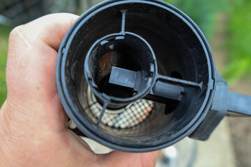 A hand holds an automotive engine component, likely a mass airflow sensor, revealing its internal...