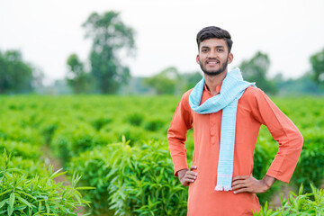 young indian farmer standing at green agricultural field