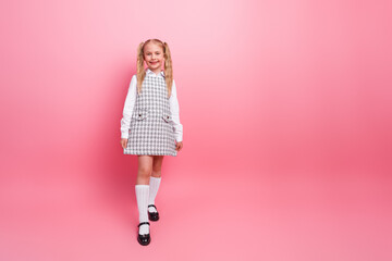 Charming primary schoolgirl wearing stylish uniform and smiling against pink background