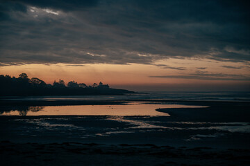 beach point of view of a basin of water during a low tide on a colorful sunrise with clouds in the sky