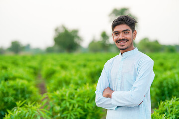 young indian farmer standing at green agricultural field