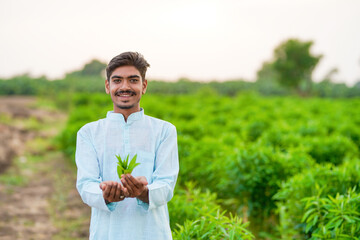 young indian farmer standing at green agricultural field