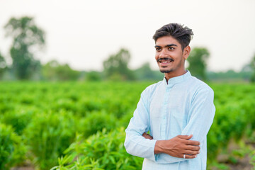 young indian farmer standing at green agricultural field