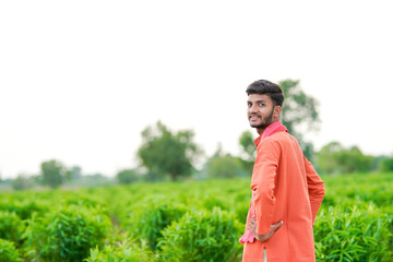young indian farmer standing at green agricultural field