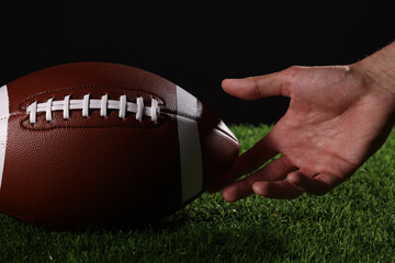Close-up of an athlete's hand playing American football, holding a football in the air on a black background