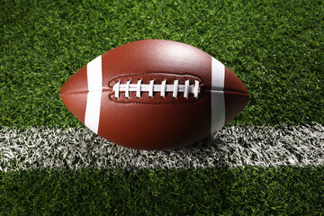 A textured American football resting on the green artificial turf with white line. College Football