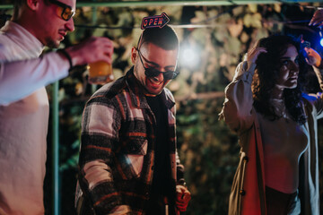 A group of friends gather together for a casual evening celebration outdoors, enjoying drinks and lively conversations under soft lighting.