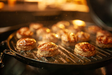 Mini burger patties sizzling on smoky barbecue grill, bite-sized meat with rising smoke