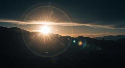 Dramatic mountain range silhouette with bright sunburst and ethereal lens flare