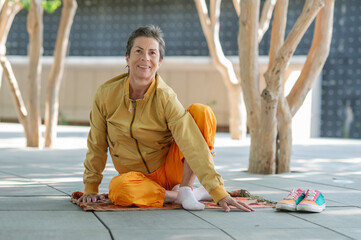 A cheerful, athletic, bright older woman does yoga outdoors in the park. Yoga is about health. Age....