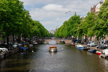 Amsterdam, Netherlands &ndash; May 21, 2025: Private boat cruising Amsterdam canal under brick arch bridge
