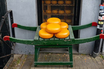 A stack of traditional Gouda cheese wheels with yellow-orange rinds, displayed on a wooden stand