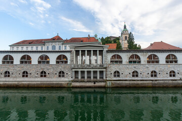 A symmetrical and iconic view of the Central Market colonnade, also known as Plechnik's Arcades, stretches along the tranquil Ljubljanica River in Ljubljana, Slovenia