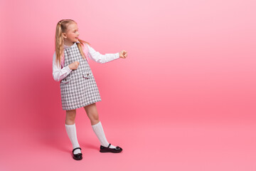 Joyful schoolgirl in a formal dress making a playful gesture on a pink background, expressing...