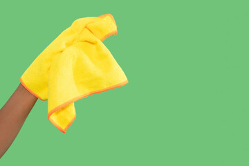 Hand holding a yellow cleaning cloth against a green background while preparing for a cleaning task...