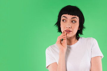Woman in a white shirt with short black hair poses thoughtfully against a bright green background...