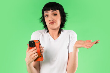 Woman with short black hair holding a phone and making a questioning gesture in front of a green...