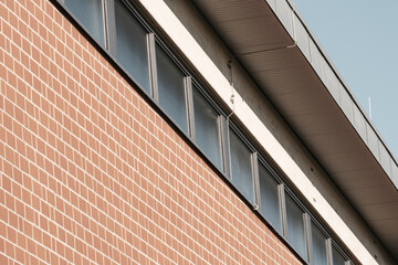 Fototapeta premium Red brick wall meeting metal roof and windows on modern building