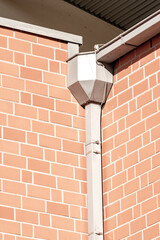 Rain gutter downspout draining water on brick wall building