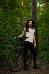 Beauty smiling sport free woman biking on bicycle on path among green woods in a summer forest...