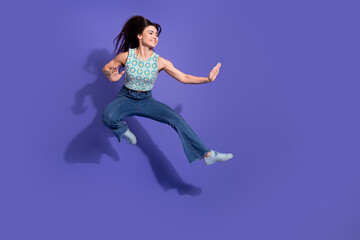 Young woman in casual attire enthusiastically jumping against a vibrant purple backdrop, showcasing...