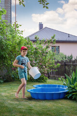 A little boy, vacationing in his grandmother's garden during the summer, prepares a small outdoor pool for swimming and refreshing himself in the cold water