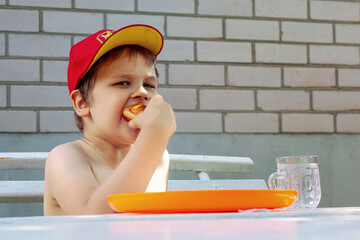 A little boy in a red cap is eating a big delicious bun