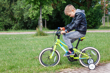 A little boy is learning to ride a bike, he concentrates on pedaling