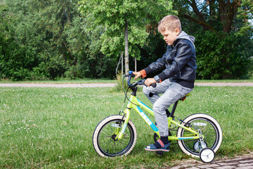 A little boy wearing a black jacket riding a yellow bicycle with white wheels