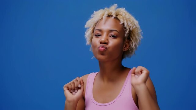 A joyful young Black woman with short blonde hair dances energetically in a pink top.