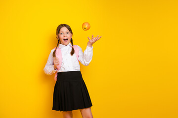 Adorable schoolgirl with backpack bouncing an apple in delight while dressed in school uniform on...