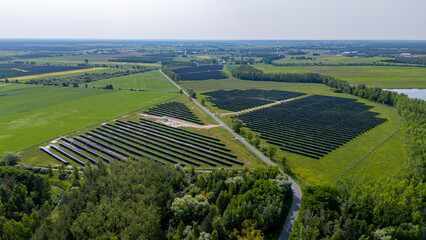 Aerial view of a solar farm in the countryside, surrounded by green fields and forest.