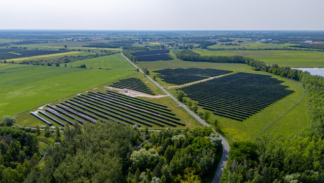 Aerial view of a solar farm in the countryside, surrounded by green fields and forest.