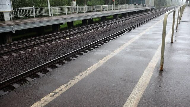 Train station with a wet track and a white line on the ground. The train station is empty and the tracks are wet from the rain