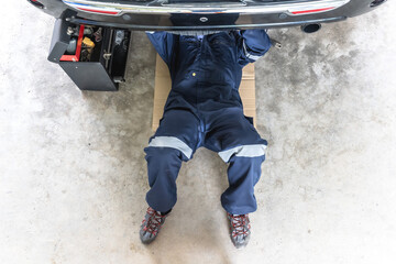 Unknown car mechanic man lying and fixing underneath car in repair shop