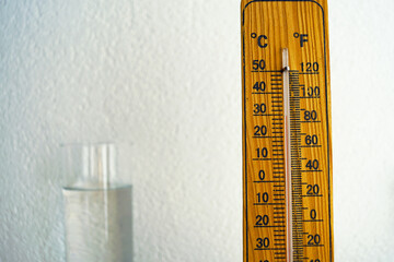 Thermometer reading elevated temperature with a glass of water in the background. Representation of...