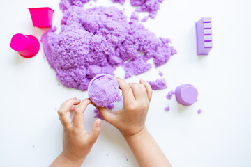 Child hands playing with purple kinetic sand and molds on white background