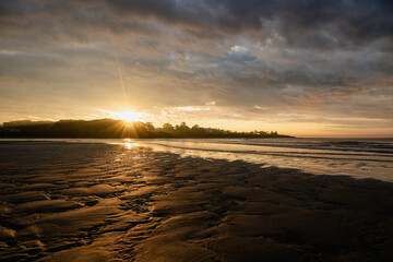view from the shore on low tides with patterned sand in the foreground with the sun rising in the...