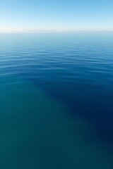 Obraz premium A serene expanse of deep blue ocean stretches to the horizon under a clear sky, its surface undisturbed and reflecting the light