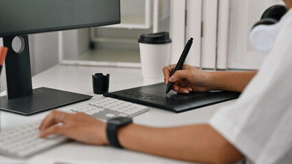 Close-up view of a woman using a stylus on a digital drawing tablet at a modern desk setup