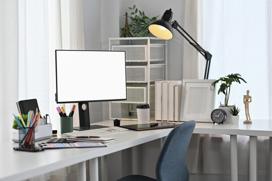 Modern creative workspace with a blank monitor, drawing tablet, color palette and coffee cup in a bright office setting