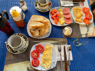 Breakfast in hotel series. Top view of healthy breakfast spread at homestay or guesthouse. Eggs, fresh fruits, bread tea and juice. Cozy, rustic setting, dining, or food concept. Trinidad, Cuba.