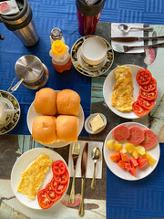 Breakfast in hotel. Vertical, top view of healthy breakfast spread at homestay or guesthouse. Eggs, fresh fruits, bread tea and juice. Cozy, rustic setting, dining, or food concept. Trinidad, Cuba.