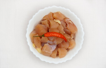 Raw chicken breast pieces on a white bowl with red chilli on top over a white background. Healthy food. Horizontal, copy space.