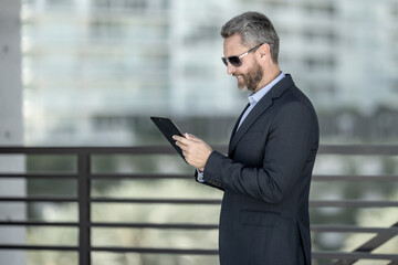 Fototapeta premium Urban entrepreneur reviewing business strategy. Business man outdoors on tablet. Business man using tablet outside. Business man checking finance data. Rich business man reviewing contract on tablet.