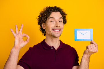 Young man showcasing a mail icon on a yellow background while smiling and gesturing an OK sign with...