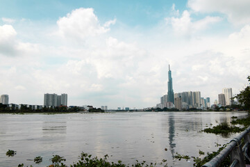 A scenic view of a river with a prominent tall skyscraper and modern buildings in the background,...